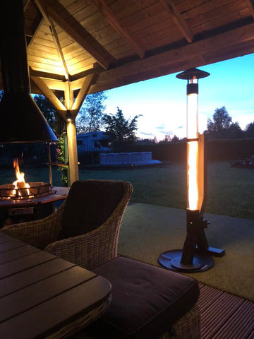 Pelletofen brennt unter einem Holzdach neben einem Feuertisch mit Blick in den Garten